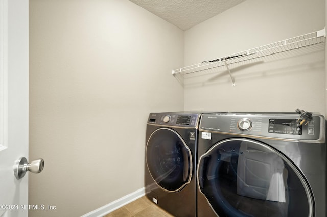 clothes washing area with washing machine and clothes dryer, light tile patterned floors, and a textured ceiling