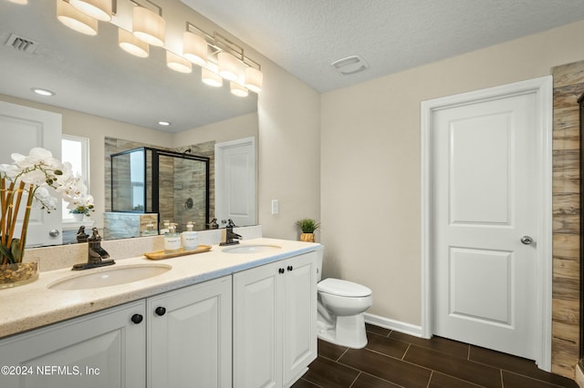 bathroom with a shower with door, vanity, a textured ceiling, and toilet