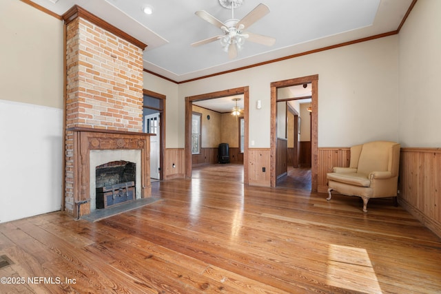 unfurnished living room with ceiling fan, a brick fireplace, crown molding, and light wood-type flooring