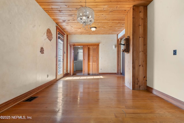 empty room with wood ceiling, light hardwood / wood-style flooring, and a notable chandelier