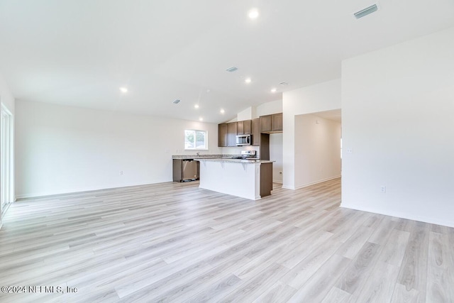 kitchen with stainless steel appliances, light hardwood / wood-style flooring, vaulted ceiling, a kitchen bar, and a kitchen island