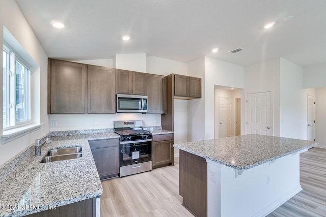 kitchen with light wood-type flooring, light stone counters, stainless steel appliances, sink, and a kitchen island