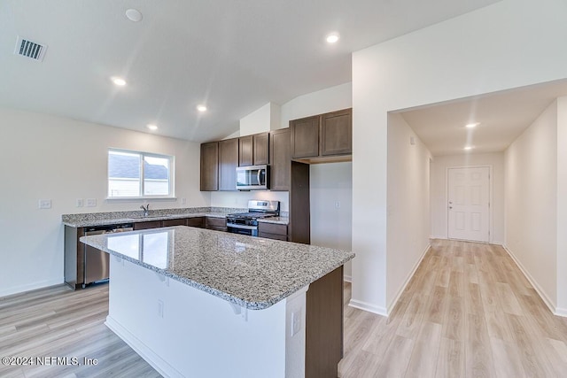 kitchen with light stone countertops, a center island, light hardwood / wood-style floors, vaulted ceiling, and appliances with stainless steel finishes