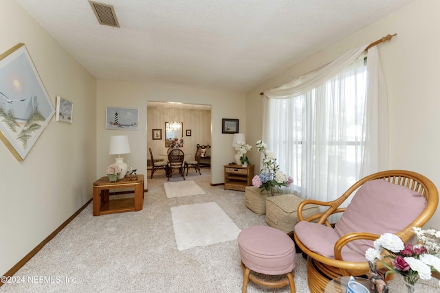 living area featuring light carpet, a textured ceiling, and an inviting chandelier