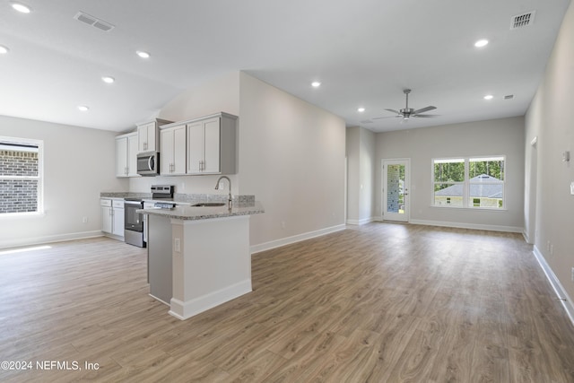 kitchen featuring appliances with stainless steel finishes, sink, ceiling fan, light stone counters, and light hardwood / wood-style flooring