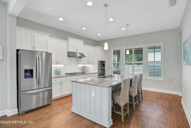 kitchen with white cabinets, a center island with sink, hanging light fixtures, light stone countertops, and appliances with stainless steel finishes