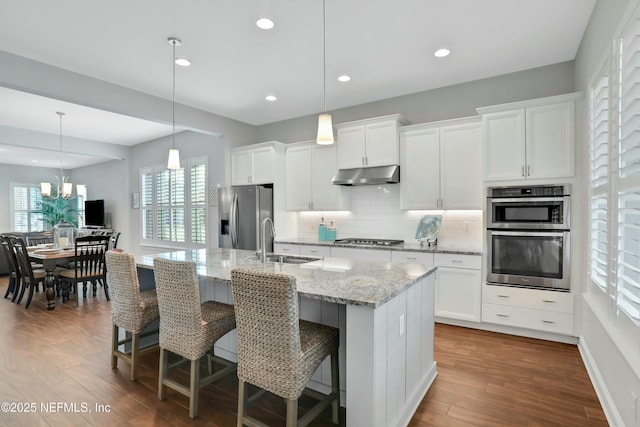 kitchen with white cabinetry, sink, stainless steel appliances, pendant lighting, and a center island with sink