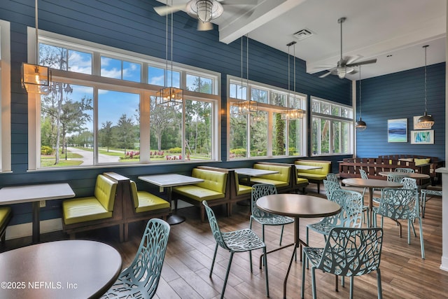 sunroom / solarium with beam ceiling, a wealth of natural light, and ceiling fan with notable chandelier