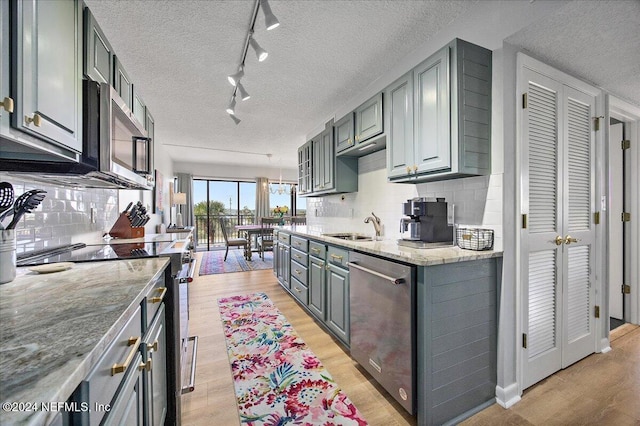 kitchen with appliances with stainless steel finishes, a textured ceiling, tasteful backsplash, and light hardwood / wood-style flooring