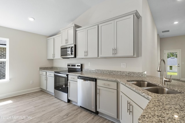 kitchen with light stone counters, stainless steel appliances, sink, and light hardwood / wood-style flooring