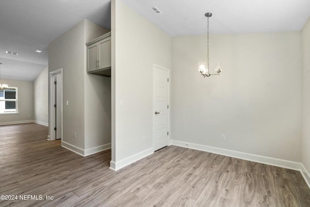 unfurnished room featuring lofted ceiling, light wood-type flooring, and a chandelier