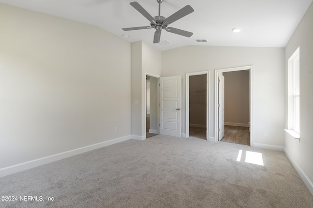 unfurnished bedroom featuring vaulted ceiling, a walk in closet, light colored carpet, and ceiling fan