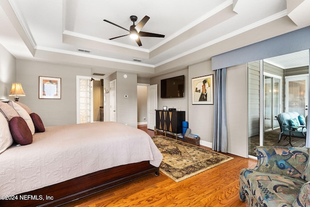 bedroom featuring a tray ceiling, visible vents, wood finished floors, and crown molding