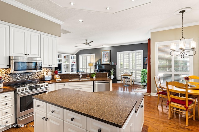 kitchen with wood finished floors, a sink, stainless steel appliances, crown molding, and open floor plan