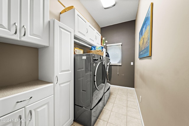 laundry area featuring light tile patterned floors, baseboards, cabinet space, and washer and clothes dryer