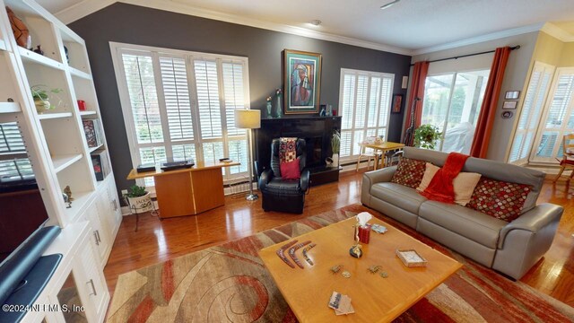 living room with wood finished floors, crown molding, and a fireplace with raised hearth