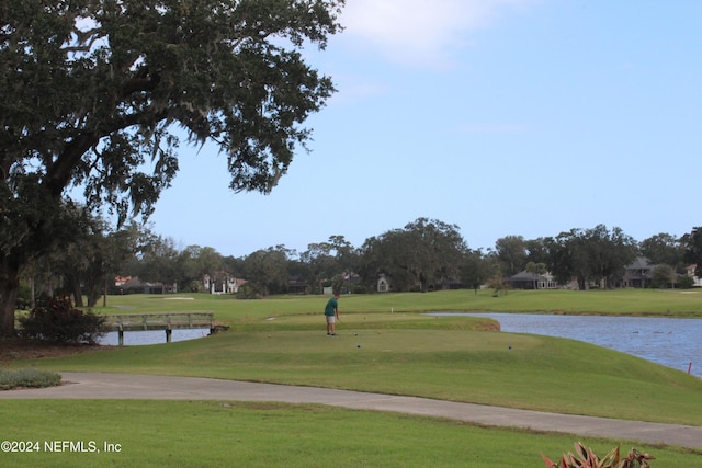 view of property's community with view of golf course, a lawn, and a water view