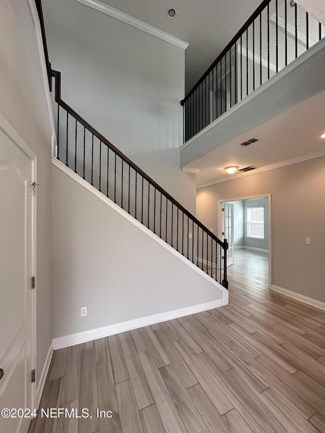 stairway featuring hardwood / wood-style floors, a towering ceiling, and ornamental molding