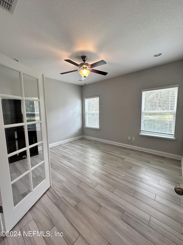 spare room featuring a textured ceiling, light hardwood / wood-style floors, a wealth of natural light, and ceiling fan