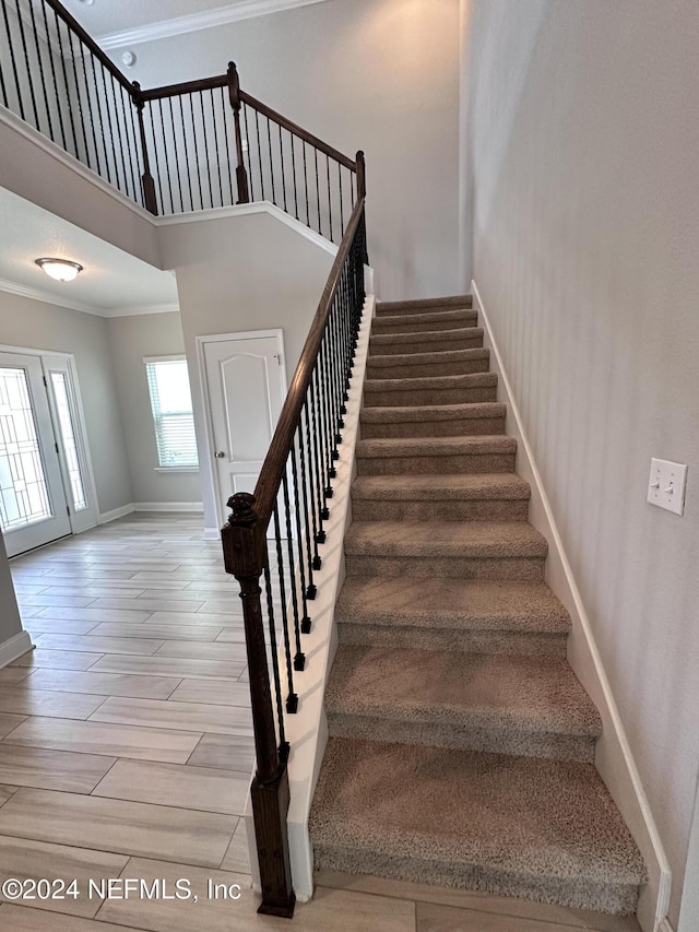 stairs featuring hardwood / wood-style floors, crown molding, and a high ceiling