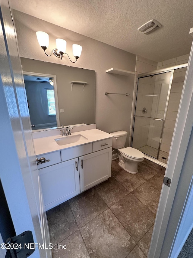 bathroom featuring vanity, toilet, a shower with shower door, and a textured ceiling