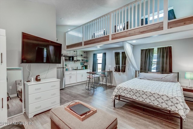 bedroom featuring stainless steel fridge, wood-type flooring, a towering ceiling, and multiple windows