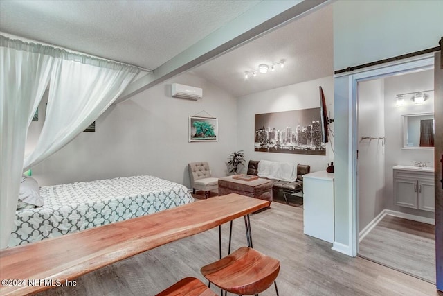 bedroom featuring lofted ceiling with beams, ensuite bath, a barn door, light wood-type flooring, and a wall unit AC