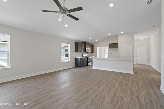 unfurnished living room featuring sink, vaulted ceiling, ceiling fan, light wood-type flooring, and a textured ceiling