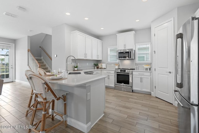 kitchen with appliances with stainless steel finishes, light hardwood / wood-style flooring, white cabinetry, and a wealth of natural light