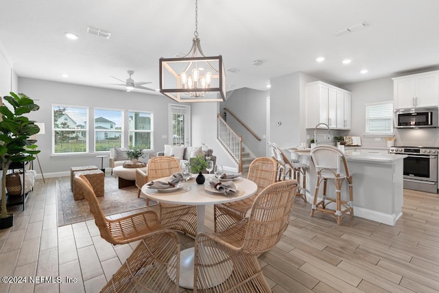 dining room featuring ceiling fan with notable chandelier and light hardwood / wood-style flooring