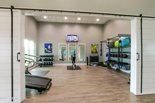 gym featuring a barn door, wood-type flooring, and a high ceiling