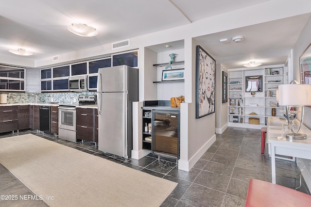 kitchen featuring dark brown cabinets, beverage cooler, backsplash, and appliances with stainless steel finishes