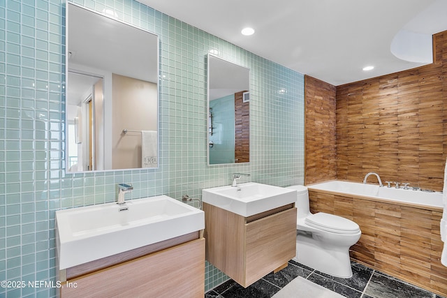 bathroom featuring vanity, a relaxing tiled tub, tile walls, and toilet