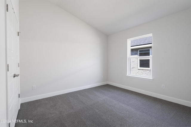 spare room featuring vaulted ceiling and dark carpet