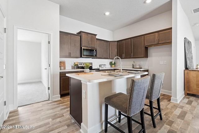 kitchen with sink, an island with sink, a textured ceiling, a breakfast bar area, and appliances with stainless steel finishes