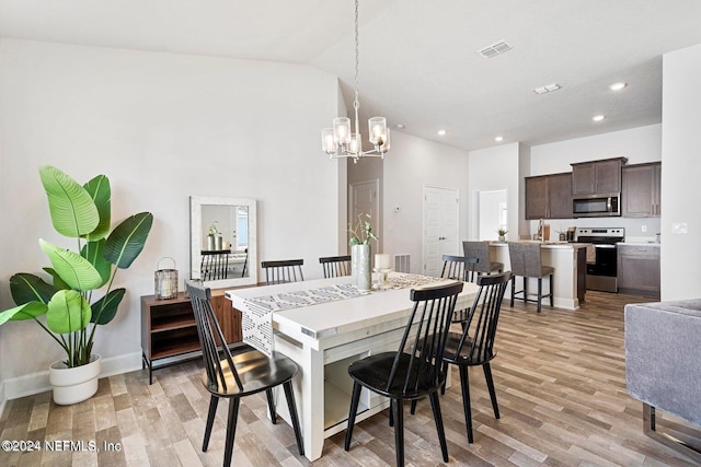 dining space with light hardwood / wood-style floors, sink, high vaulted ceiling, and an inviting chandelier