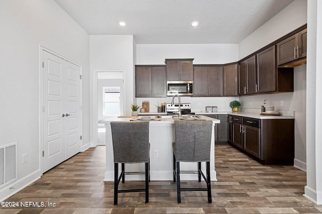 kitchen with a center island with sink, dark hardwood / wood-style floors, dark brown cabinetry, and appliances with stainless steel finishes