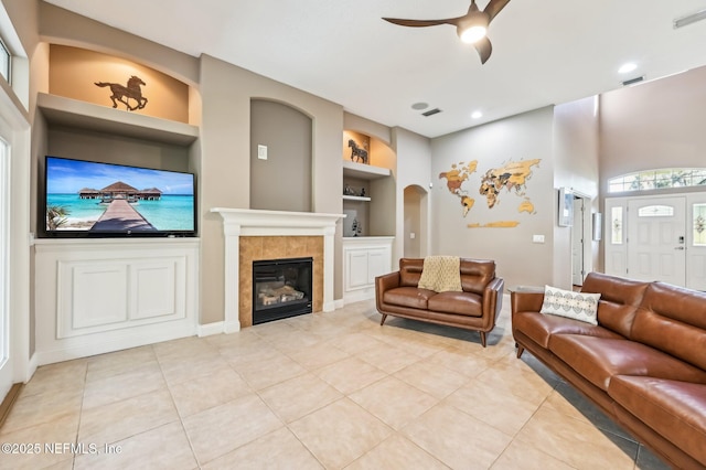 living room with a tile fireplace, ceiling fan, built in features, and light tile patterned flooring