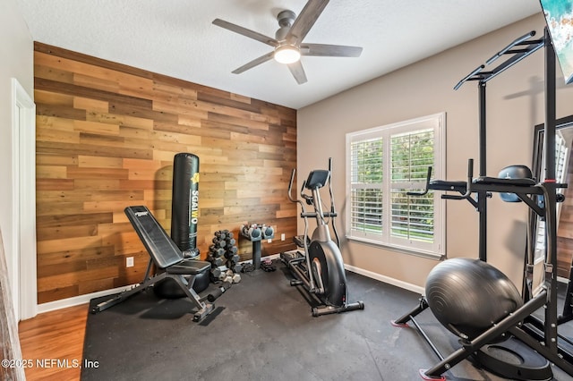 exercise room with a textured ceiling, ceiling fan, and wooden walls