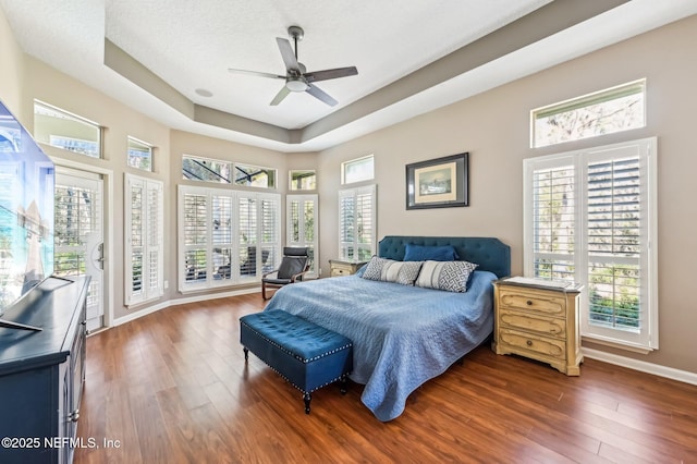 bedroom with a textured ceiling, dark hardwood / wood-style floors, a raised ceiling, and ceiling fan