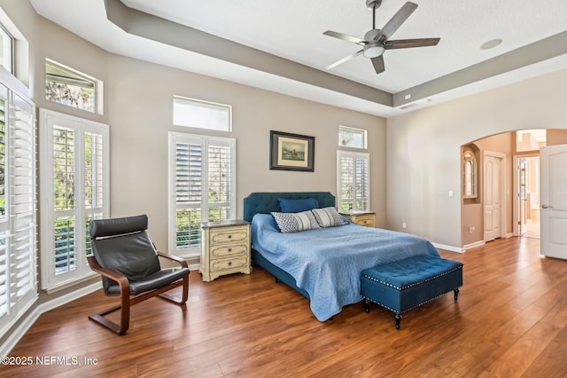 bedroom with hardwood / wood-style floors, a textured ceiling, a raised ceiling, and ceiling fan