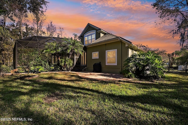 back house at dusk with a lanai, a yard, and a patio