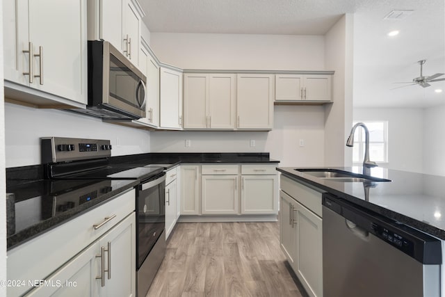 kitchen with ceiling fan, sink, stainless steel appliances, light hardwood / wood-style flooring, and dark stone counters