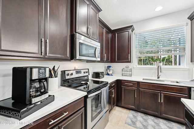 kitchen featuring dark brown cabinets, sink, light tile patterned floors, and stainless steel appliances