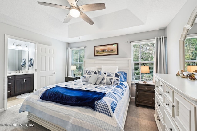 bedroom featuring light carpet, a tray ceiling, ensuite bath, and ceiling fan