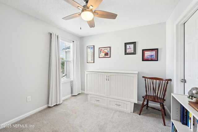 living area with a textured ceiling, light colored carpet, and ceiling fan