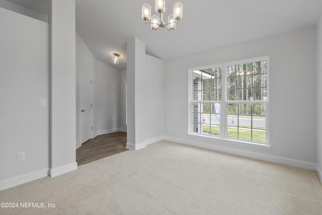 carpeted spare room featuring a notable chandelier and vaulted ceiling