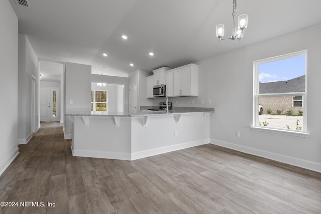 kitchen with stainless steel appliances, wood-type flooring, lofted ceiling, a kitchen bar, and white cabinets