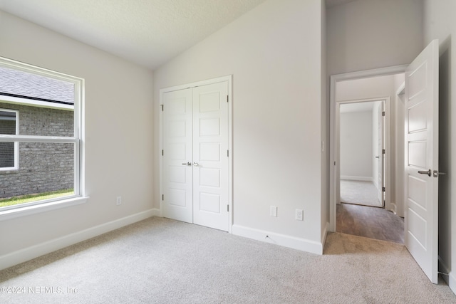 unfurnished bedroom featuring a textured ceiling, light colored carpet, vaulted ceiling, and a closet