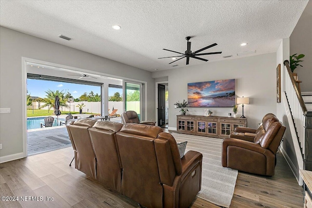 living room with a textured ceiling, light hardwood / wood-style floors, and ceiling fan